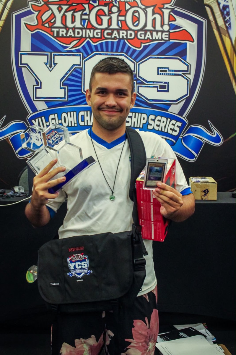 Rafael Reich, o ReichYGO, segurando troféus e cartas num Yu-Gi-Oh! Championship Series